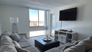 Una sala de estar moderna con un sofá seccional, una mesa de centro, un televisor de pantalla plana montado en la pared y una estantería.