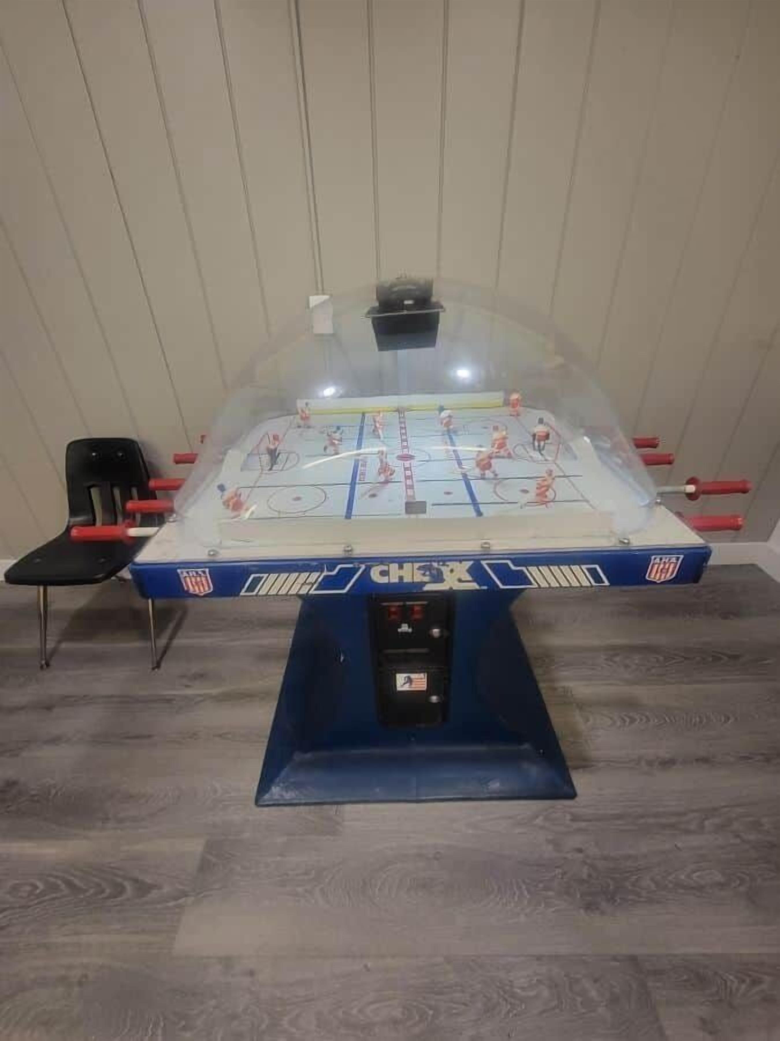 Une table de baby-foot avec un socle bleu et un couvercle transparent, entourée de chaises.
