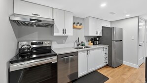A modern kitchen with white cabinets, stainless steel appliances, and a black kettle on the stove. - Bright & Modern 2BR Basement Suite w/ Rustic Bar & Private Entrance (Kingston)