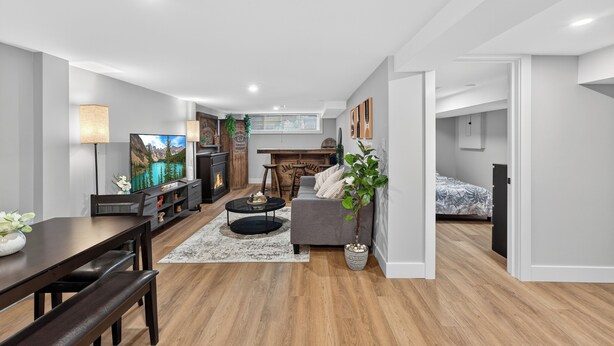 A modern living room with a fireplace, a dining area, and a bedroom. - Bright & Modern 2BR Basement Suite w/ Rustic Bar & Private Entrance (Kingston)