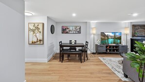 A modern living room with a dining table, a flat-screen TV, and a fireplace. - Bright & Modern 2BR Basement Suite w/ Rustic Bar & Private Entrance (Kingston)
