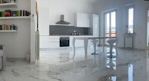 A modern kitchen with white cabinetry, a built-in oven, and a dining area with two bar stools.