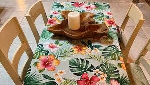 Ruokapöytä, jonka päällä on kukallinen pöytäliina, ja pöydän ympärillä on puisia tuoleja.
