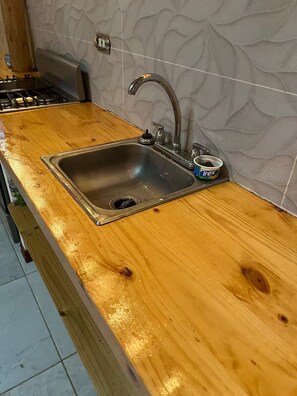 A kitchen with a stainless steel sink, wooden countertop, and a textured backsplash.