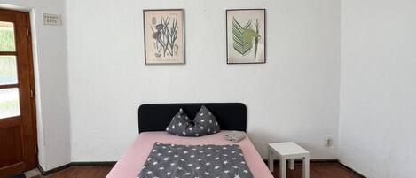 A bedroom with a bed, a small bedside table, and two framed botanical prints on the wall.