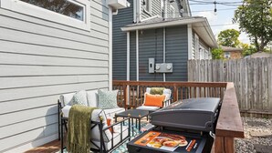 A wooden deck with outdoor furniture, a barbecue grill, and a view of a house with a blue exterior. - NEW, Designer Home Sleeps 10, King Beds, Deck + Blackstone Grill (Indianapolis)