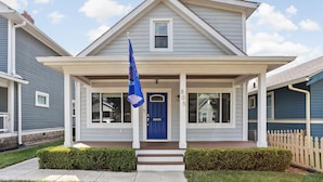 A two-story house with a blue front door, a covered porch, and a picket fence. - NEW, Designer Home Sleeps 10, King Beds, Deck + Blackstone Grill (Indianapolis)