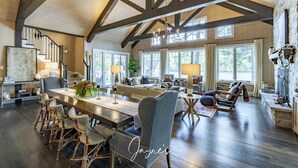 A spacious living room with a high ceiling, wooden beams, a large dining table, and comfortable seating.
