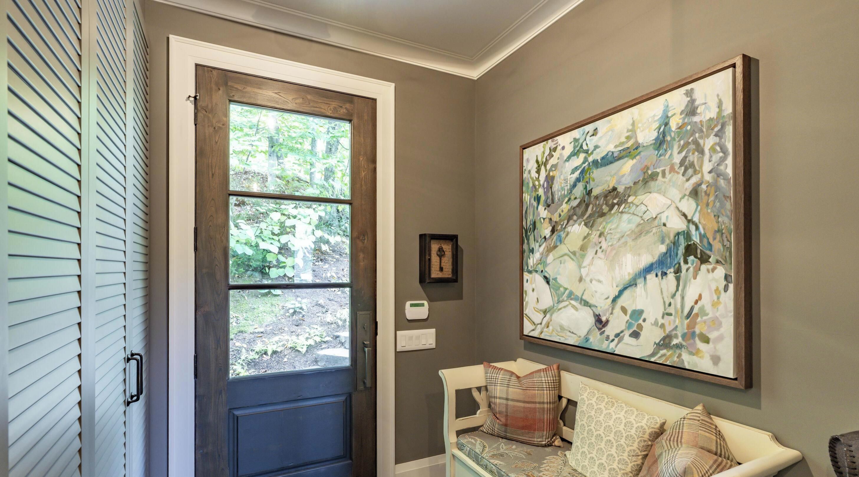 A room with a door leading to a garden, a large abstract painting on the wall, and a bench with cushions.