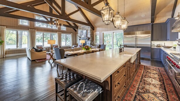 A spacious living area with a large island, wooden beams, and a view of the outdoors.