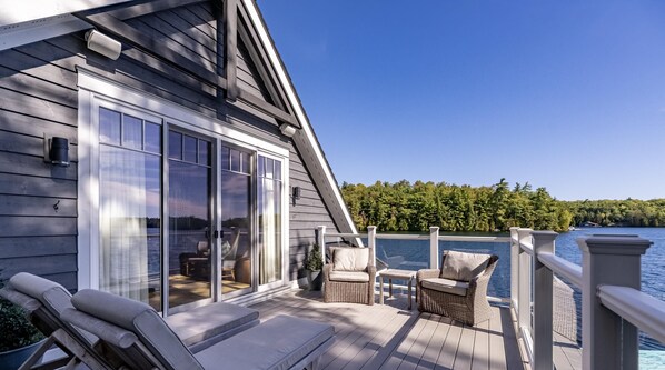 A wooden deck with lounge chairs, a wicker chair, and a glass door leading to an interior space.