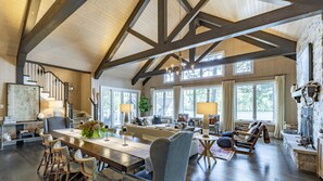 Un salon spacieux avec un plafond haut, des poutres apparentes, une grande table à manger et des sièges confortables.