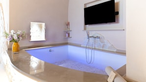 A modern bathroom with a built-in bathtub, a mounted television, and a small shelf with decorative items. - Bed and Breakfast 'Super Luxury' with Private Garden, Wi-Fi and Air Conditioning (Massafra)