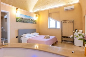 Un dormitorio con cama, ventana, cuadro, toalla, banco y florero.
