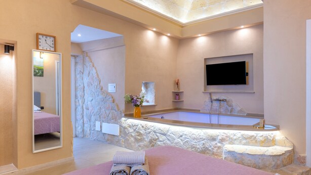 A modern bathroom with a stone wall, a large bathtub, a mirror, and a flat-screen TV. - Bed and Breakfast 'Super Luxury' with Private Garden, Wi-Fi and Air Conditioning (Massafra)