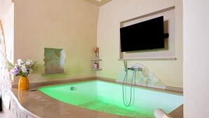A spa area with a green-lit pool, a mounted TV, and a stone wall. - Bed and Breakfast 'Super Luxury' with Private Garden, Wi-Fi and Air Conditioning (Massafra)