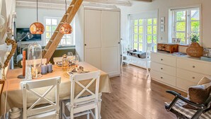 Uma área de refeições com uma mesa de madeira posta para dois, cadeiras brancas e um armário branco com gavetas.