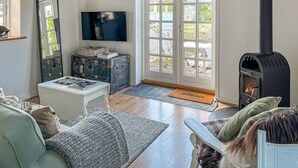 Uma sala de estar aconchegante com lareira, televisão e uma grande janela com vista para um jardim.