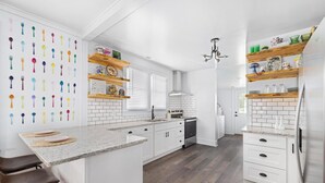 Una cocina moderna con armarios blancos, una isla central, estantes de madera y un salpicadero.