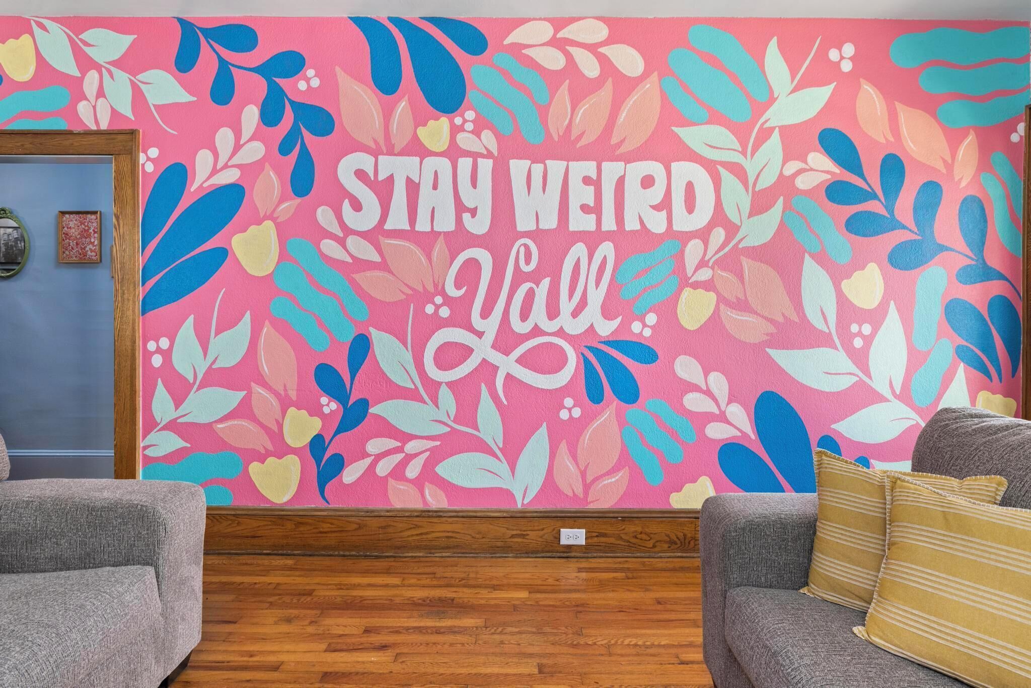 Una habitación con un vibrante mural floral, dos sofás grises y un suelo de madera.