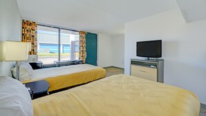 A hotel room with two beds, a TV, a desk, and a window with curtains.