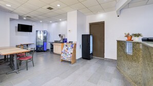 A clean, modern lobby with a reception desk, seating area, vending machine, and a refrigerator.