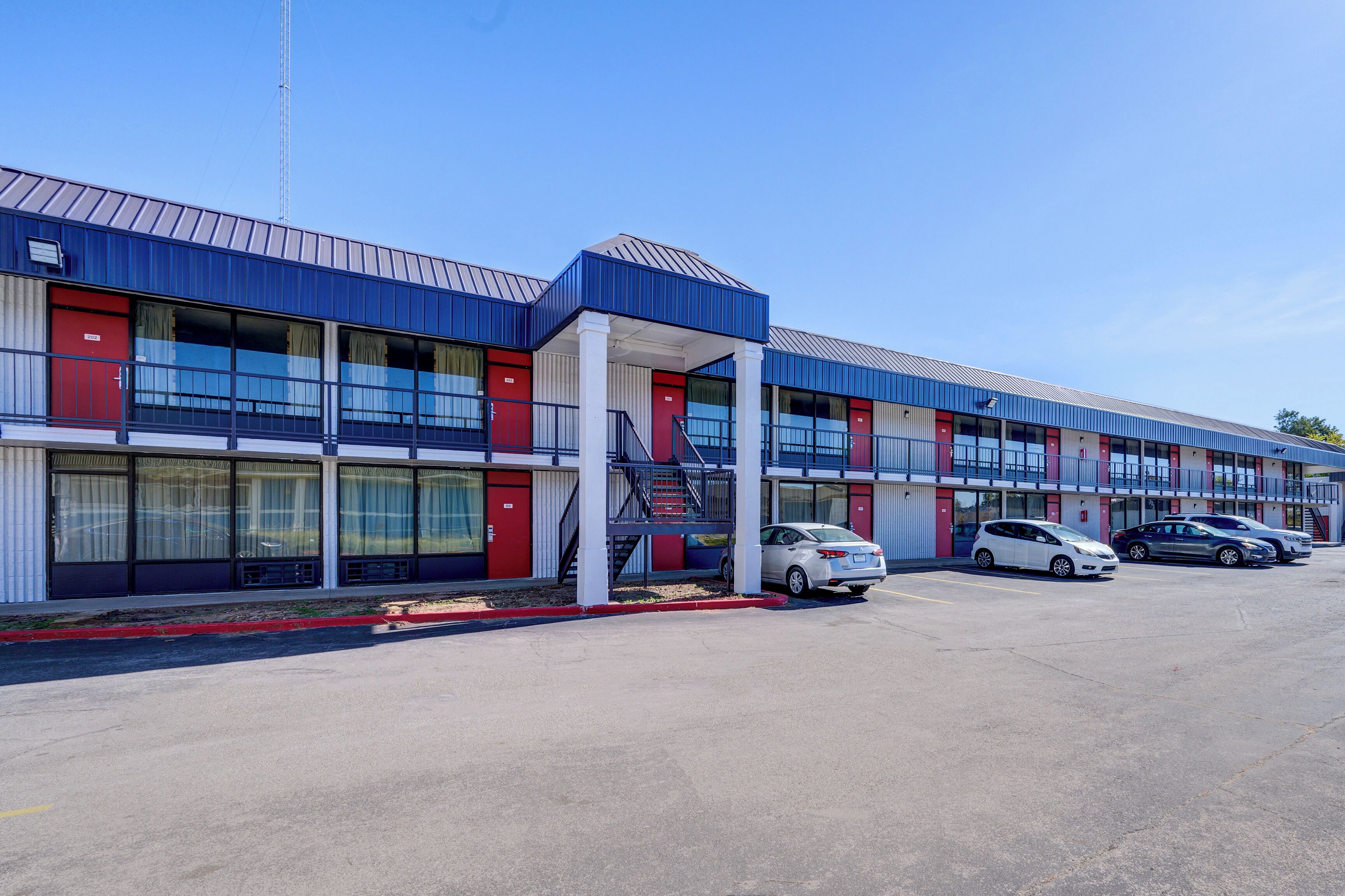 Un motel à plusieurs étages, avec une façade bleue et rouge, un espace de stationnement couvert et plusieurs voitures garées devant.