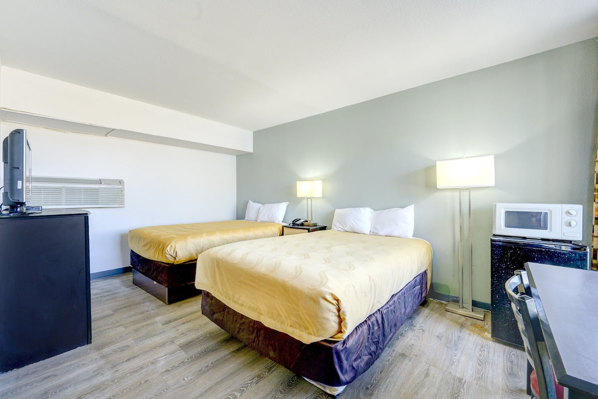 A hotel room with two beds, a desk, a microwave, and a lamp.