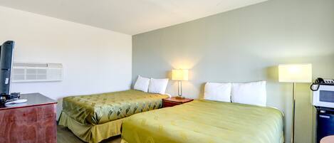 A hotel room with two beds, a desk, a TV, and a desk lamp.