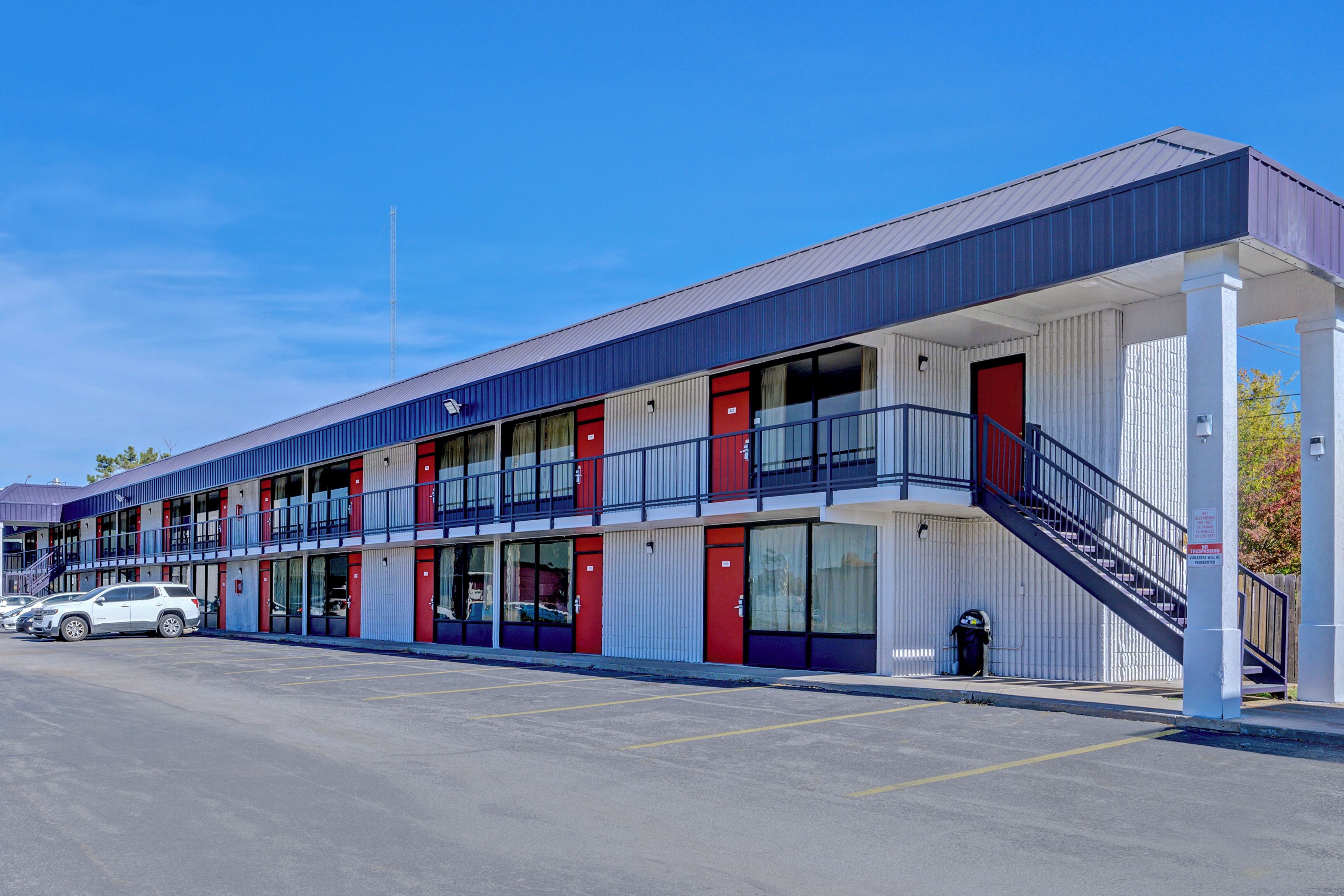 A motel with a two-story structure, multiple rooms with red doors, a covered walkway, and a parking lot.