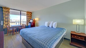 A hotel room with a large bed, a desk with a chair, a nightstand, and a view through the window.