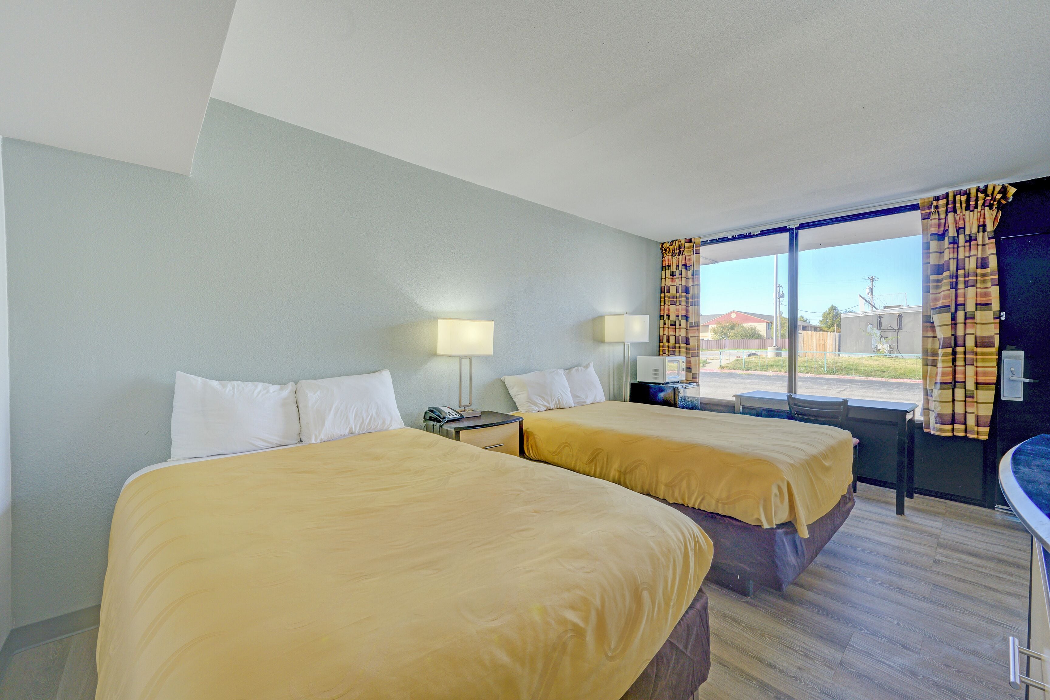 Habitación de hotel con dos camas, un escritorio, una silla, un ventanal con cortinas y vistas al exterior.