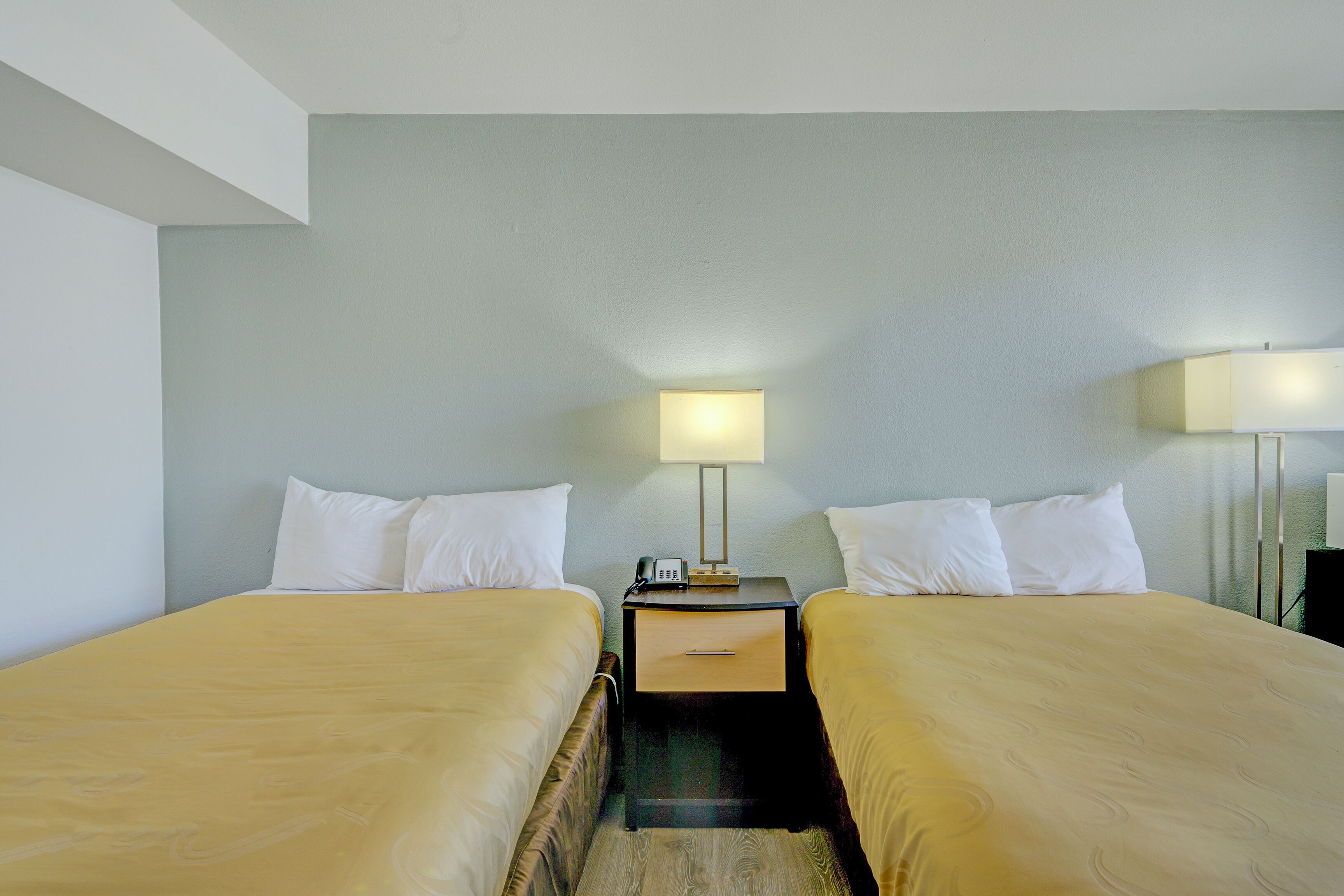 A hotel room with two beds, a nightstand with a lamp, and a small table.