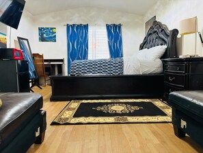 Een slaapkamer met een bed, een bureau, een stoel, een dressoir, een televisie en een schilderij aan de muur.