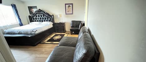 Un dormitorio con cama, sofá, sillón, mesita de noche y un cuadro en la pared.