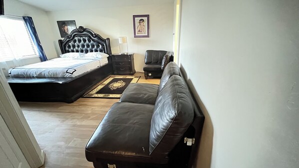 A bedroom with a bed, a sofa, a chair, a nightstand, and a wall-mounted picture.