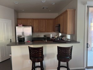 A kitchen with wooden cabinets, a stainless steel refrigerator, a microwave, and two bar stools. - Spacious 5-bedroom house in gorgeous Tucson with AC (Tucson)