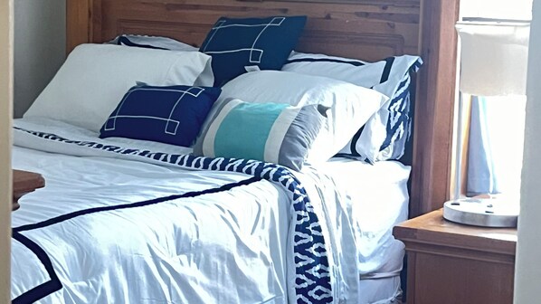 A bed with a wooden headboard, white and blue bedding, and a bedside table with a lamp.