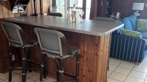 A kitchen with a bar area, wooden walls, and a tiled floor. - Classic Beachfront Home on Gulf of Mexico at TWIN PEAKS now with Elevator (Saint George Island)