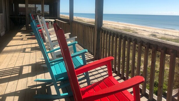 A covered outdoor seating area with wooden deck and railings, overlooking a beach. - Classic Beachfront Home on Gulf of Mexico at TWIN PEAKS now with Elevator (Saint George Island)