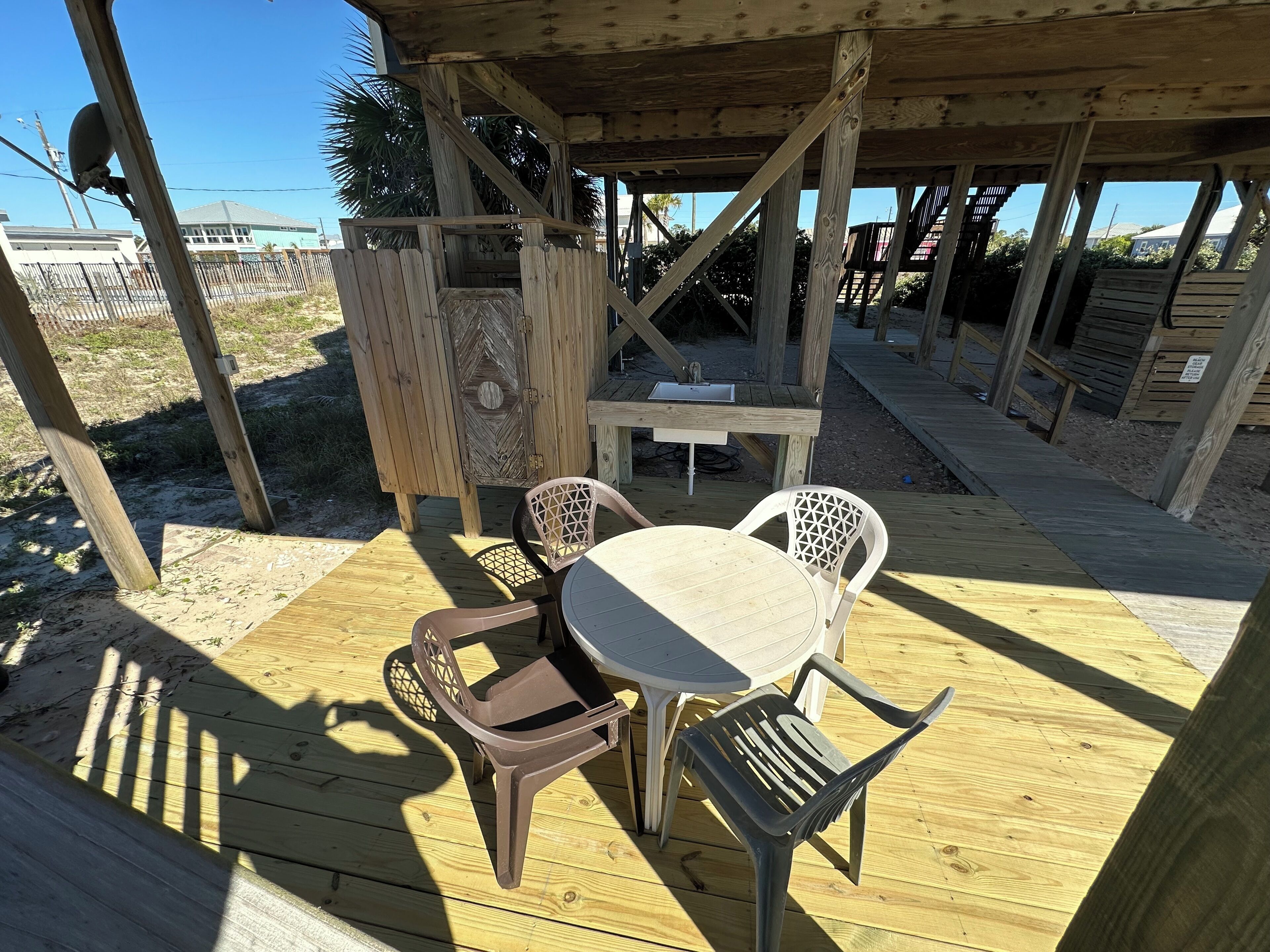 Une terrasse en bois avec une table et des chaises, une clôture en bois et une vue sur la plage.