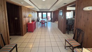 A spacious hallway with wooden walls and tiled flooring, leading to a dining area with a view of the sea. - Classic Beachfront Home on Gulf of Mexico at TWIN PEAKS now with Elevator (Saint George Island)
