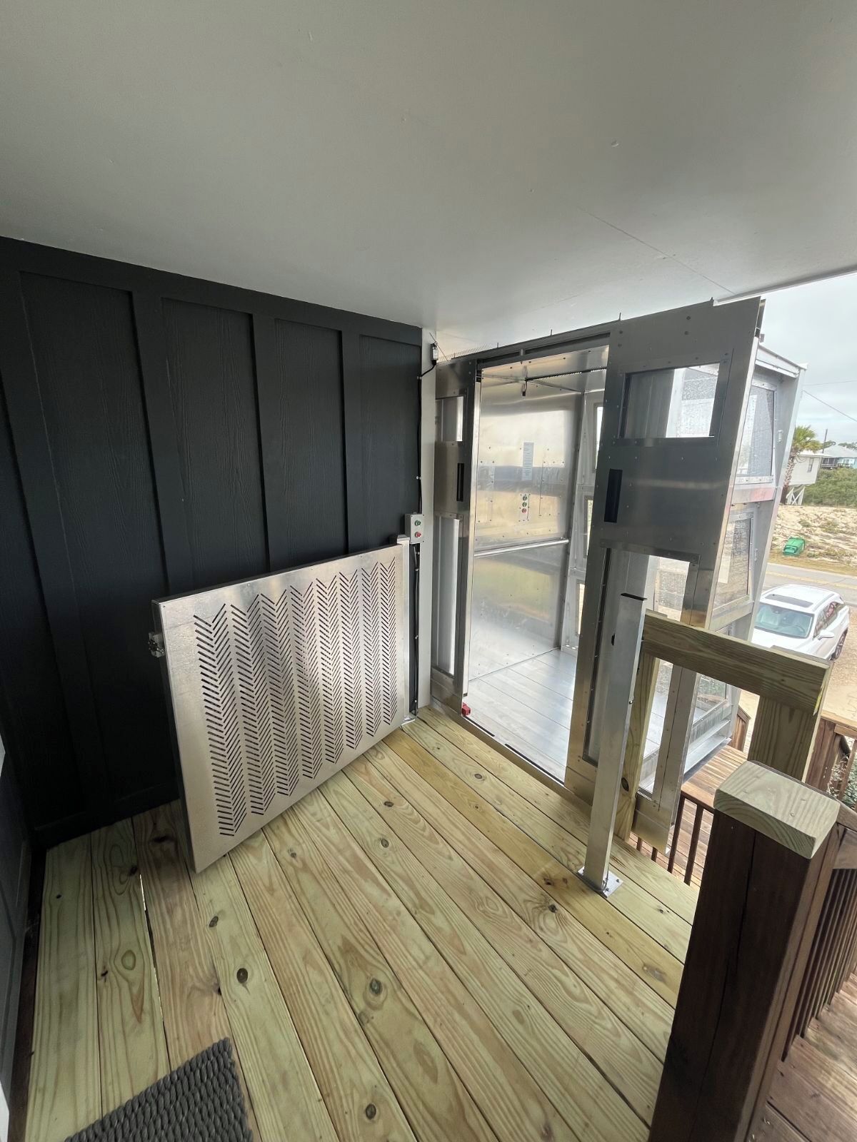 A room with a wooden floor, a black wall, and a sliding glass door leading outside.