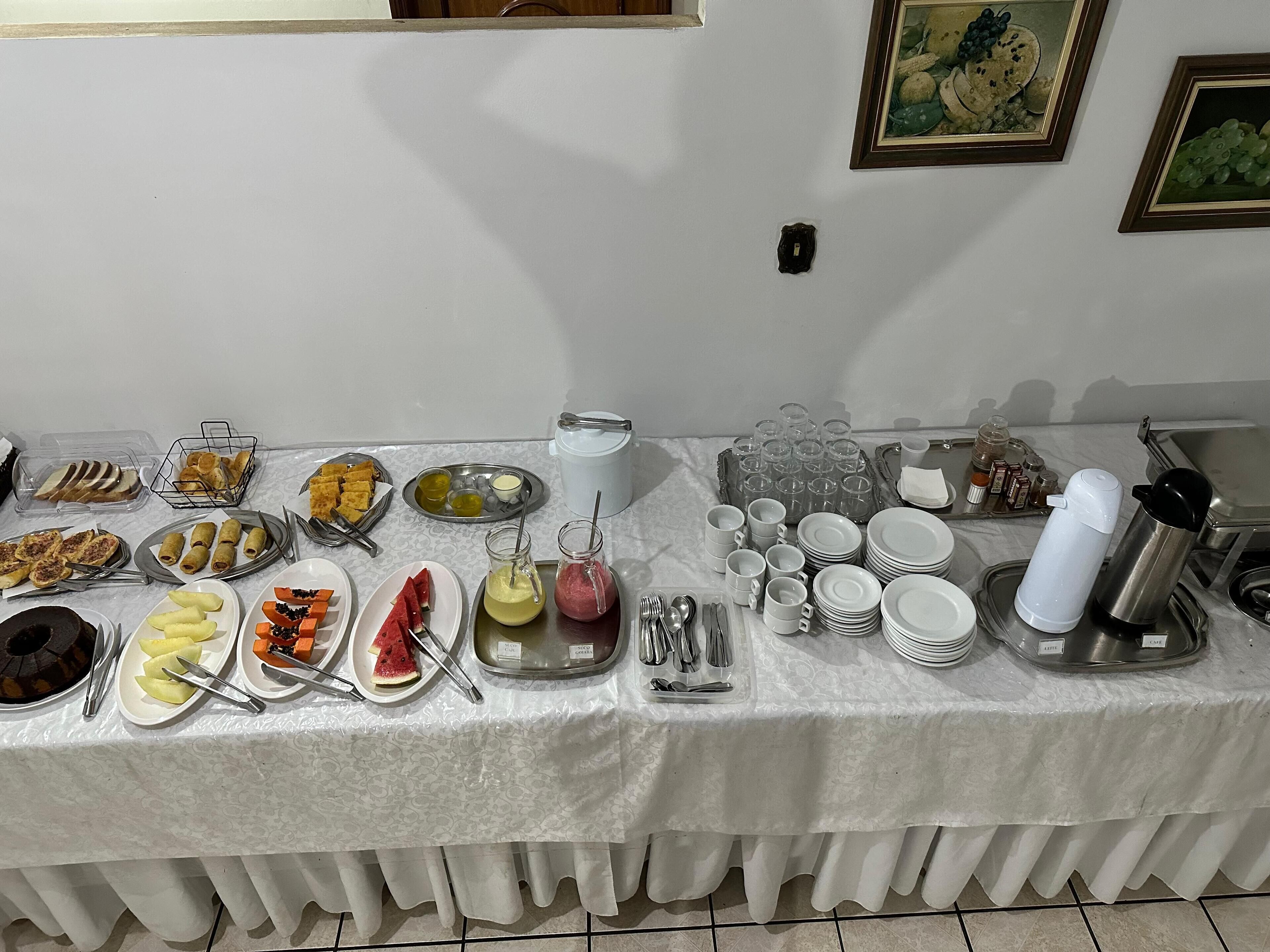 A buffet table with various food items and utensils, including plates of fruit, pastries, and condiments.