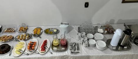 A buffet table with various food items and utensils, including plates of fruit, pastries, and condiments.