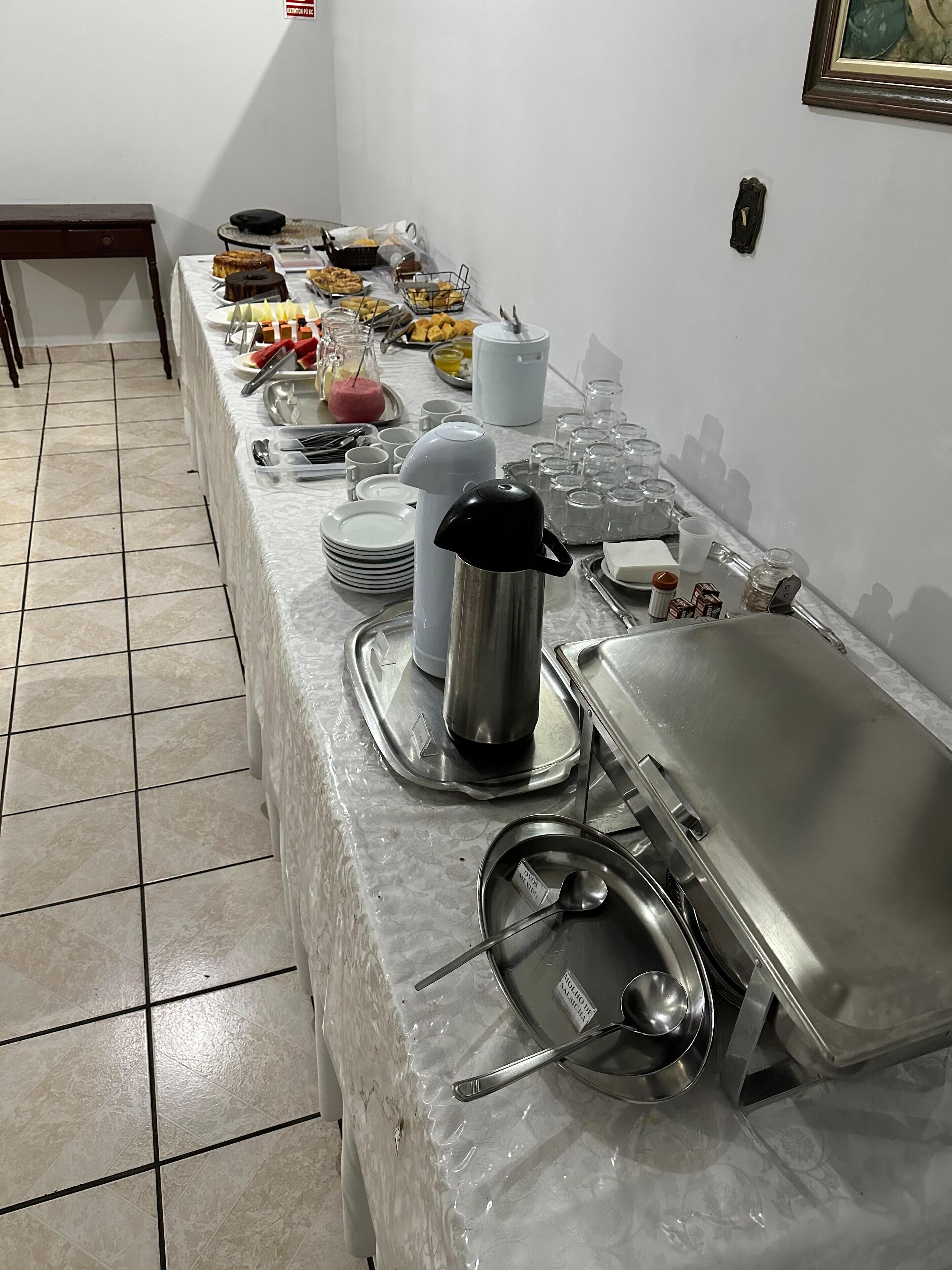 Montaje de bufé con diversos alimentos, utensilios de servicio y recipientes sobre una mesa cubierta con un protector.