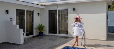 A poolside area with a pool, a white building with numbered doors, and a potted plant.