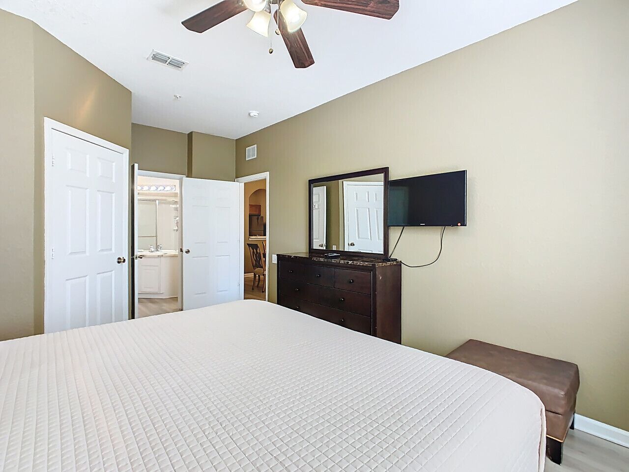 A bedroom with a large bed, a dresser, a mirror, and a ceiling fan.