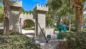A stone archway with a chain gate, surrounded by greenery and palm trees. - Windsor Hills Themed Condo Resort Pool By Disney (Kissimmee)