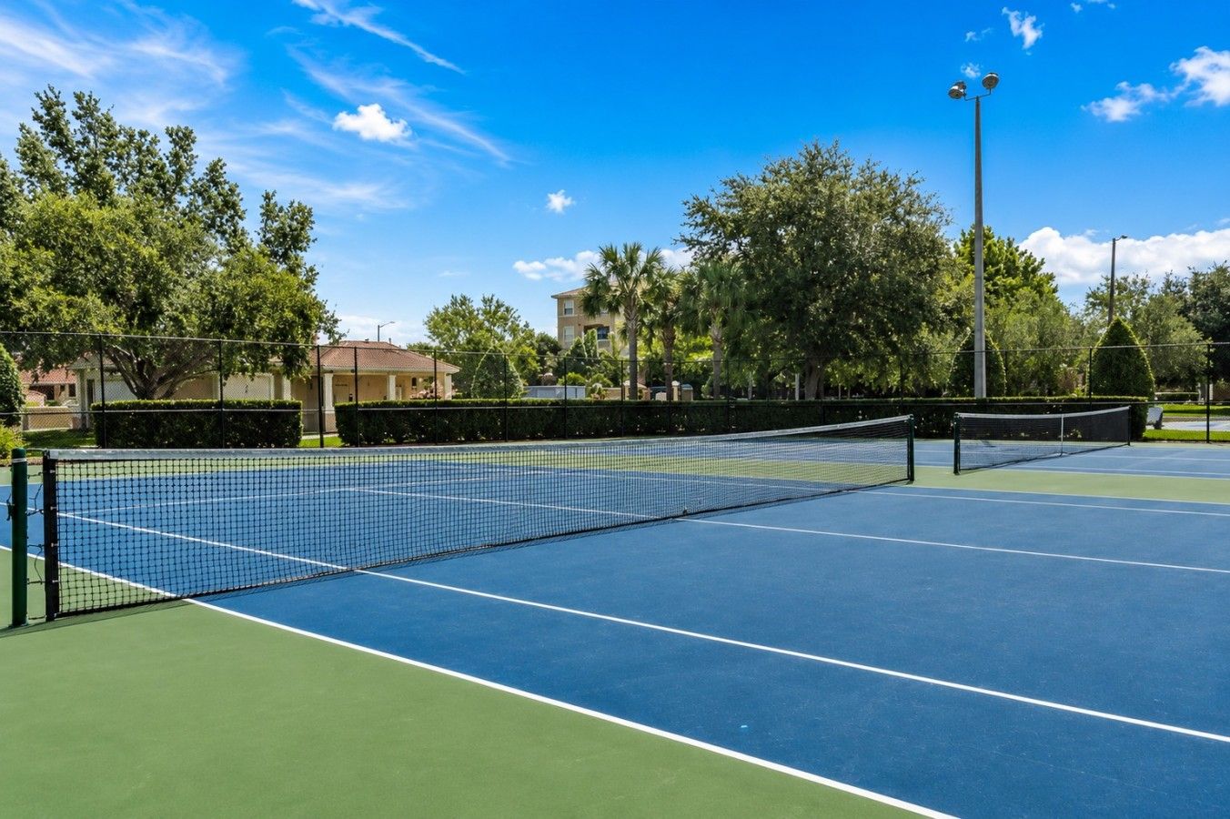 A tennis court with a net, surrounded by trees and buildings.